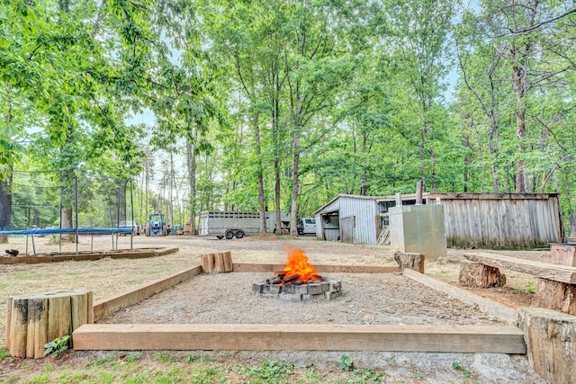 view of yard featuring fence, a trampoline, an outdoor structure, and a fire pit