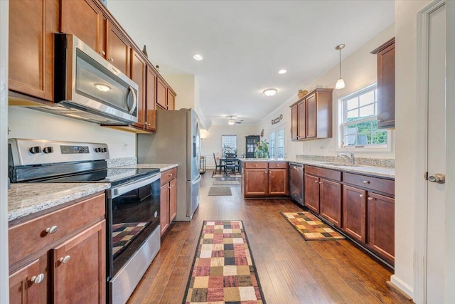 kitchen featuring decorative light fixtures, a sink, a peninsula, appliances with stainless steel finishes, and dark wood-style floors