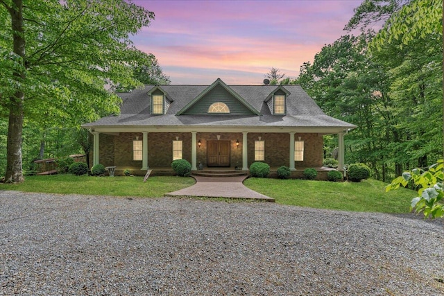 view of front of home with a porch, a shingled roof, a front lawn, and brick siding