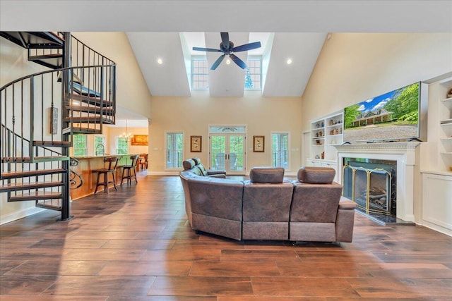 living area with a fireplace, high vaulted ceiling, stairs, a ceiling fan, and wood finished floors