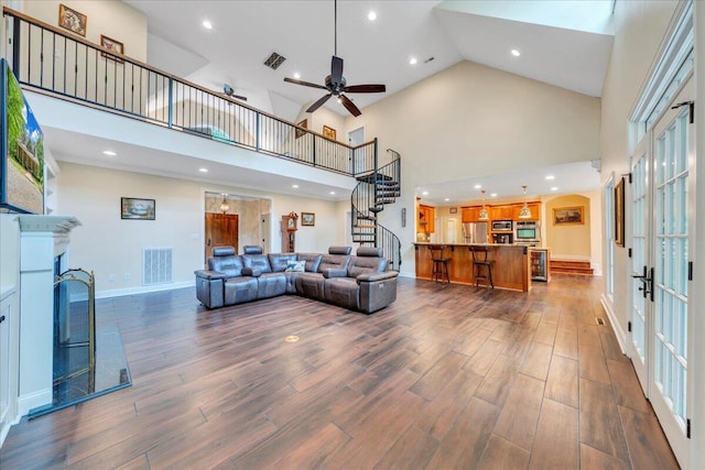 living area featuring dark wood-style flooring, visible vents, a fireplace, stairway, and high vaulted ceiling