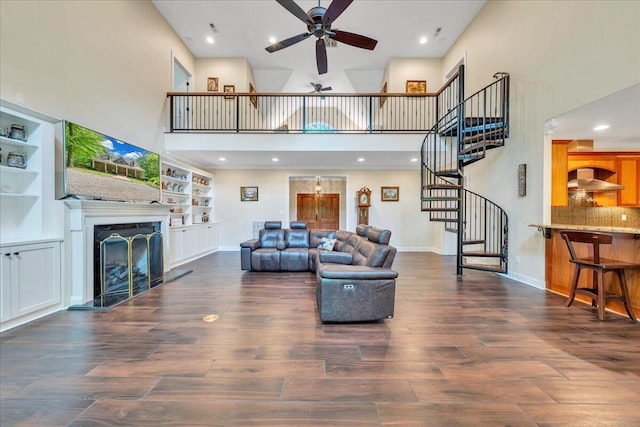 living area with stairs, wood finished floors, a high ceiling, a fireplace with raised hearth, and a ceiling fan