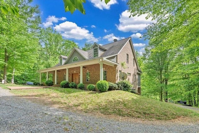 view of side of property with covered porch, brick siding, and a shingled roof