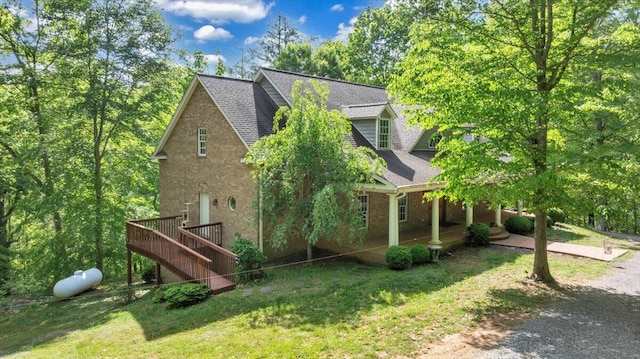 view of property exterior featuring a deck, roof with shingles, stairs, brick siding, and a yard