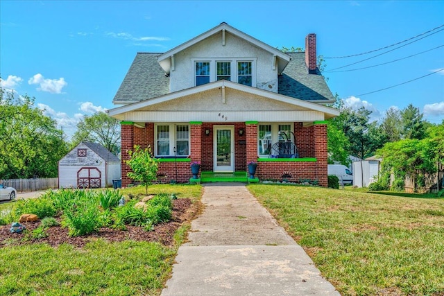 view of front of house featuring a shed, a porch, brick siding, a chimney, and an outbuilding