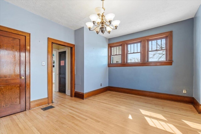 empty room featuring a chandelier, light wood-style flooring, baseboards, and a textured ceiling