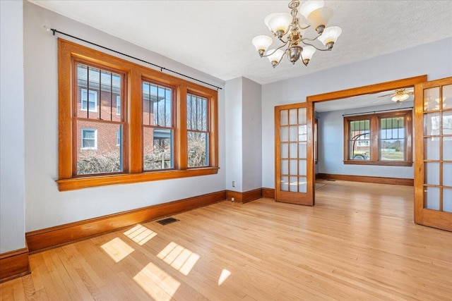 unfurnished dining area with baseboards, light wood-style flooring, french doors, and a chandelier