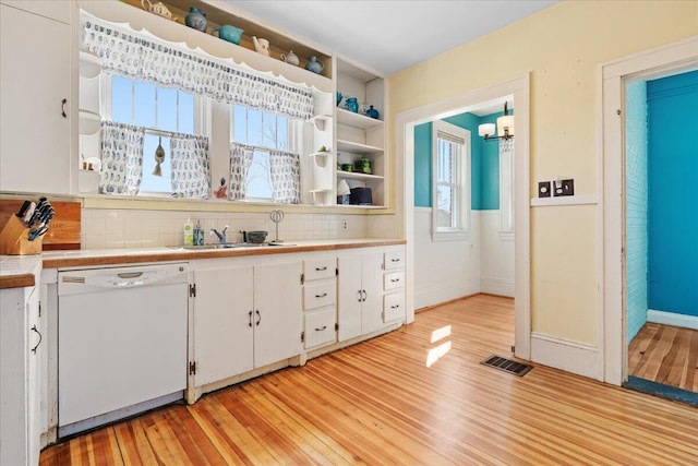 kitchen featuring white dishwasher, a sink, white cabinetry, light wood-style floors, and tasteful backsplash