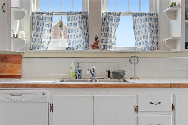 kitchen featuring dishwasher, a sink, tile counters, backsplash, and white cabinetry