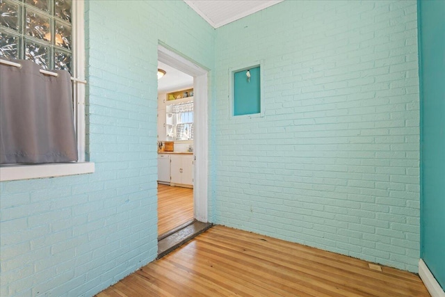 corridor with light wood-style flooring and brick wall