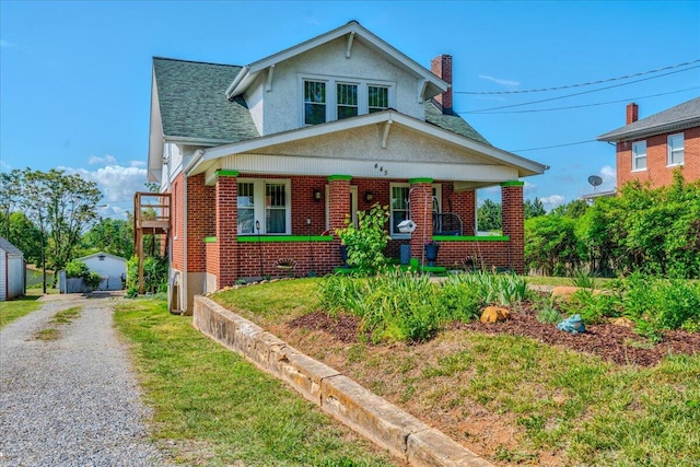 view of front of property featuring brick siding, a chimney, covered porch, a shingled roof, and driveway