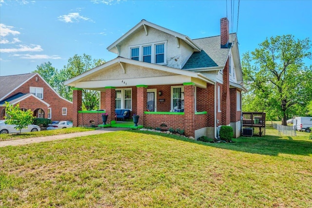 view of front of house featuring a chimney, a porch, brick siding, a front yard, and cooling unit