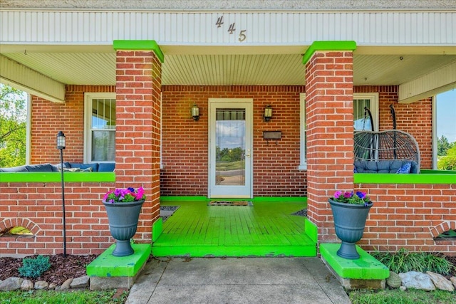 view of exterior entry featuring brick siding and covered porch