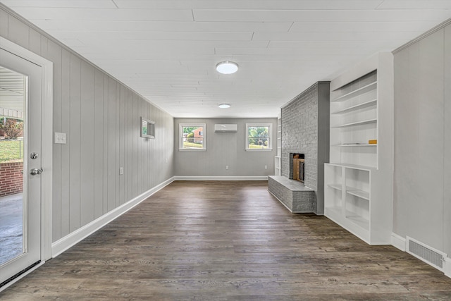 unfurnished living room featuring a wall unit AC, a brick fireplace, visible vents, dark wood-style flooring, and built in features