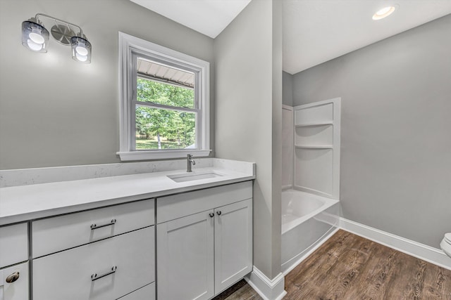 full bathroom featuring toilet, wood finished floors, a tub to relax in, baseboards, and vanity