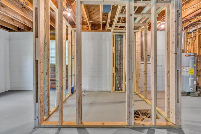 miscellaneous room with water heater, concrete block wall, and concrete floors