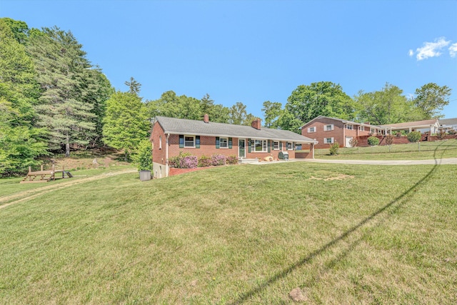 view of front facade featuring a chimney, driveway, brick siding, a patio area, and a front lawn