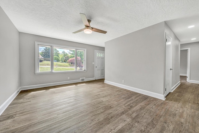 spare room with a textured ceiling, visible vents, wood finished floors, and ceiling fan