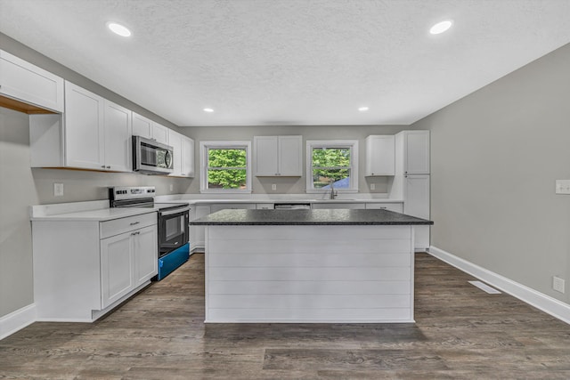 kitchen featuring a sink, electric range, white cabinets, stainless steel microwave, and a kitchen island