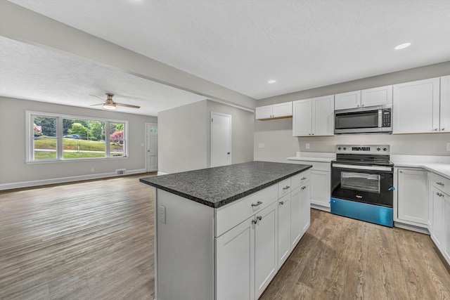 kitchen featuring light wood finished floors, open floor plan, white cabinets, electric range oven, and stainless steel microwave