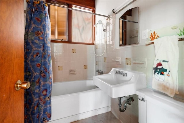 bathroom featuring toilet, a sink, tile patterned floors, tile walls, and shower / bathtub combination with curtain