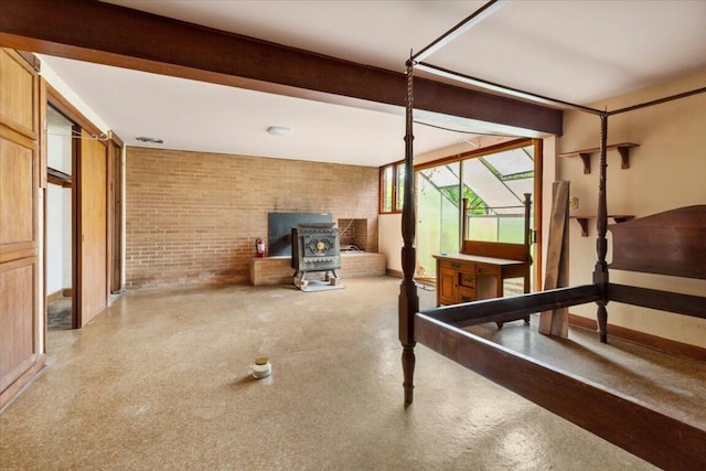 unfurnished bedroom with baseboards, a wood stove, and brick wall