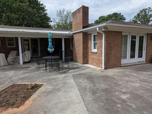 back of house featuring a patio, a chimney, metal roof, outdoor dining area, and brick siding