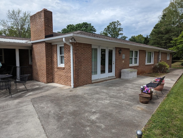 rear view of property featuring brick siding, a patio, and a chimney
