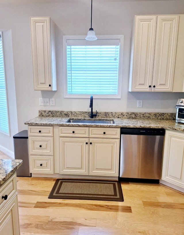 kitchen featuring a sink, stainless steel dishwasher, light wood-type flooring, and light stone counters