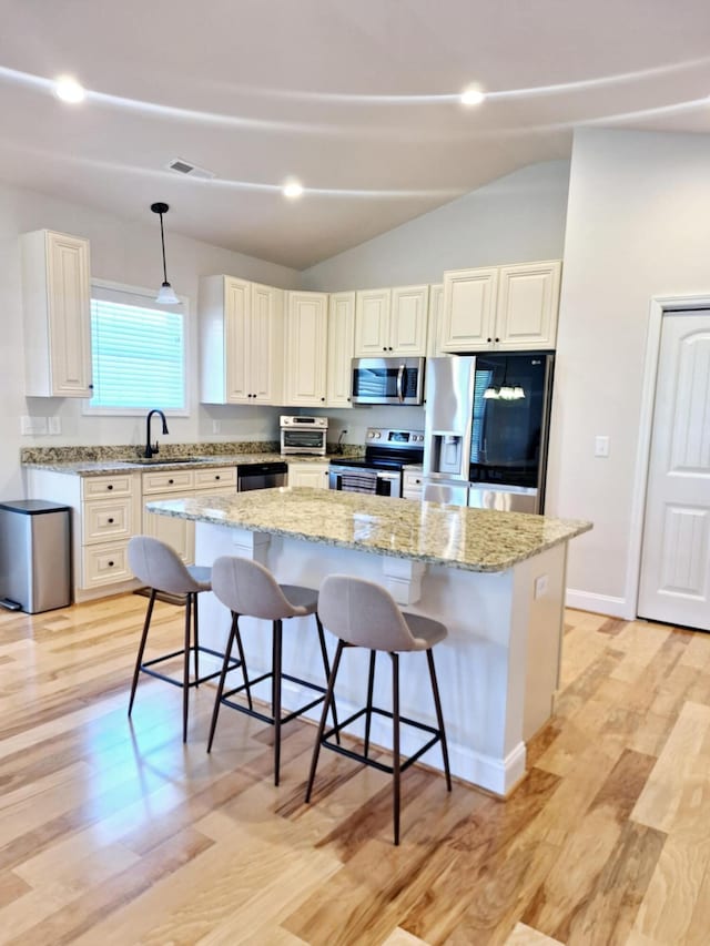kitchen featuring a breakfast bar, a kitchen island, a sink, vaulted ceiling, and stainless steel appliances
