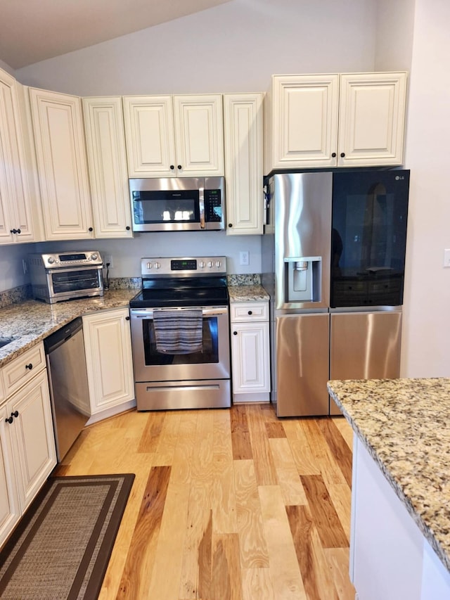 kitchen with light wood-style flooring, a toaster, stainless steel appliances, vaulted ceiling, and light stone counters