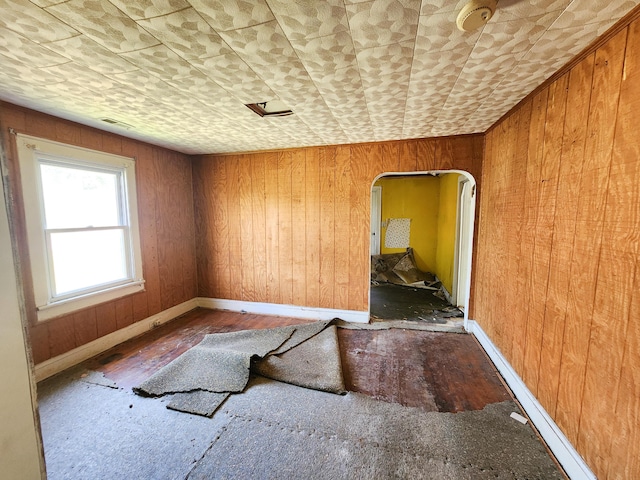 empty room with wooden walls, arched walkways, baseboards, and wood finished floors