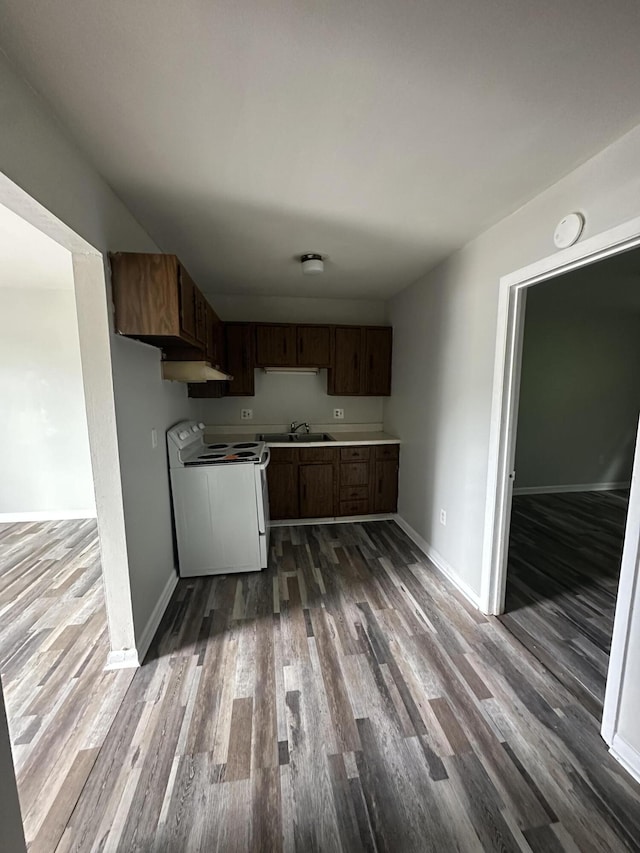 kitchen with baseboards, white range with electric stovetop, dark wood finished floors, a sink, and light countertops