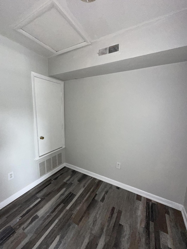 empty room featuring attic access, baseboards, dark wood-type flooring, and visible vents