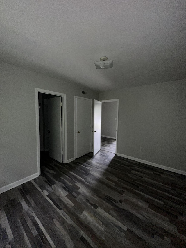 empty room featuring a textured ceiling, baseboards, and dark wood-style floors