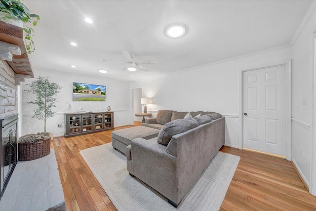 living area featuring ceiling fan, light wood-style floors, a stone fireplace, ornamental molding, and recessed lighting