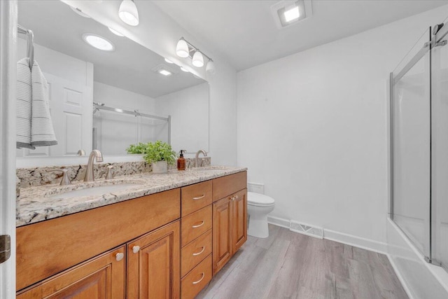 full bath with an enclosed shower, wood finished floors, double vanity, toilet, and baseboards