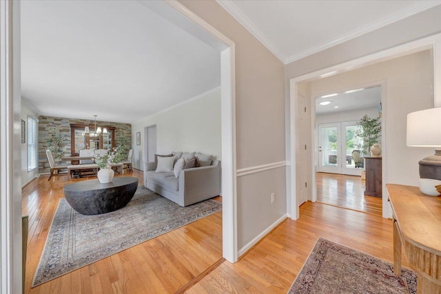 living room featuring light wood finished floors, ornamental molding, baseboards, french doors, and a chandelier