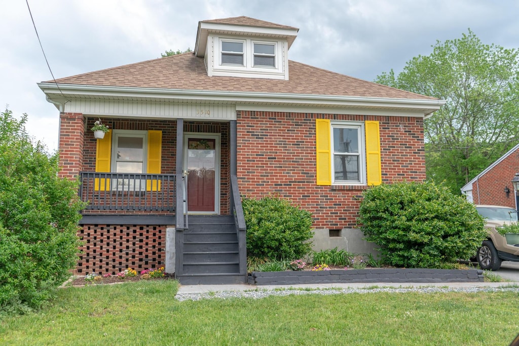 bungalow with covered porch, brick siding, a front lawn, and roof with shingles