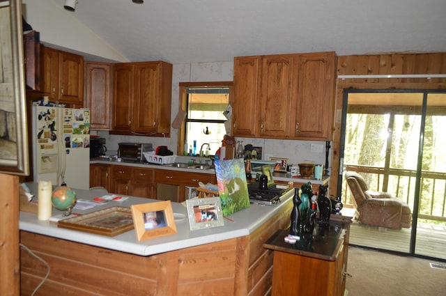 kitchen featuring white fridge with ice dispenser, lofted ceiling, brown cabinetry, a sink, and light countertops