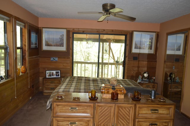 home office featuring dark colored carpet, a textured ceiling, ceiling fan, and wood walls