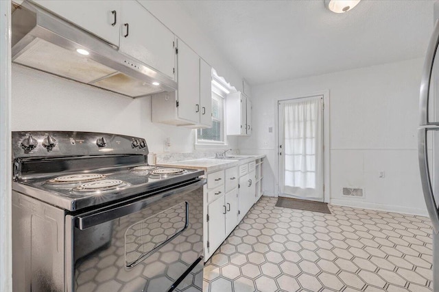1218 Grayson Ave NW, Roanoke, VA 24017 - kitchen with black / electric stove, light countertops, under cabinet range hood, white cabinets, and light floors