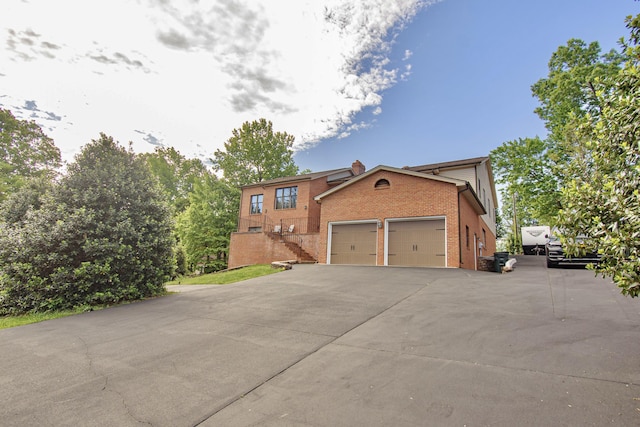 view of front of property featuring brick siding, a garage, driveway, and a chimney