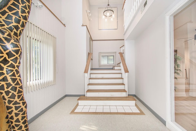 stairs featuring a towering ceiling, plenty of natural light, a chandelier, baseboards, and carpet flooring