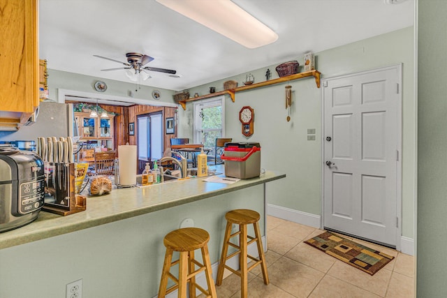 kitchen featuring light tile patterned flooring, ceiling fan, a kitchen breakfast bar, baseboards, and a peninsula