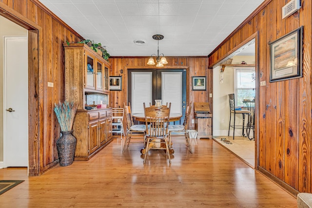 dining room with wood walls, a chandelier, light wood-type flooring, and baseboards