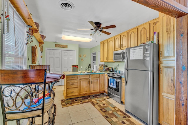 kitchen featuring appliances with stainless steel finishes, a peninsula, a sink, ceiling fan, and light tile patterned floors