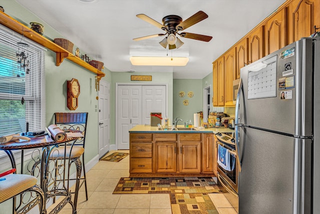 kitchen featuring appliances with stainless steel finishes, a peninsula, ceiling fan, brown cabinetry, and light countertops
