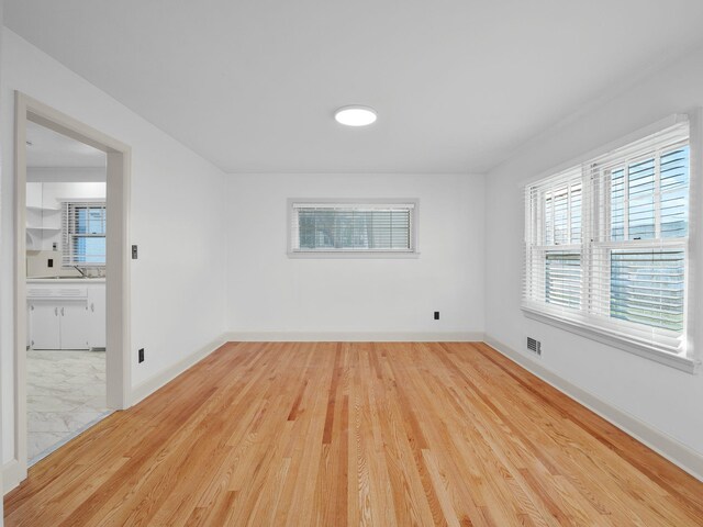 unfurnished room with wood finished floors, plenty of natural light, a sink, and baseboards
