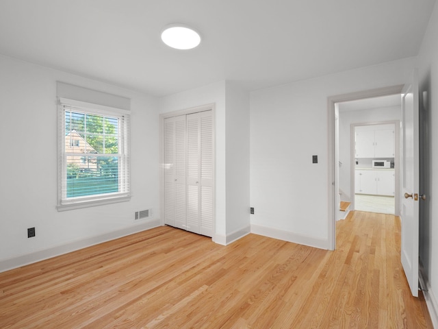 unfurnished bedroom featuring light wood-type flooring, baseboards, and a closet